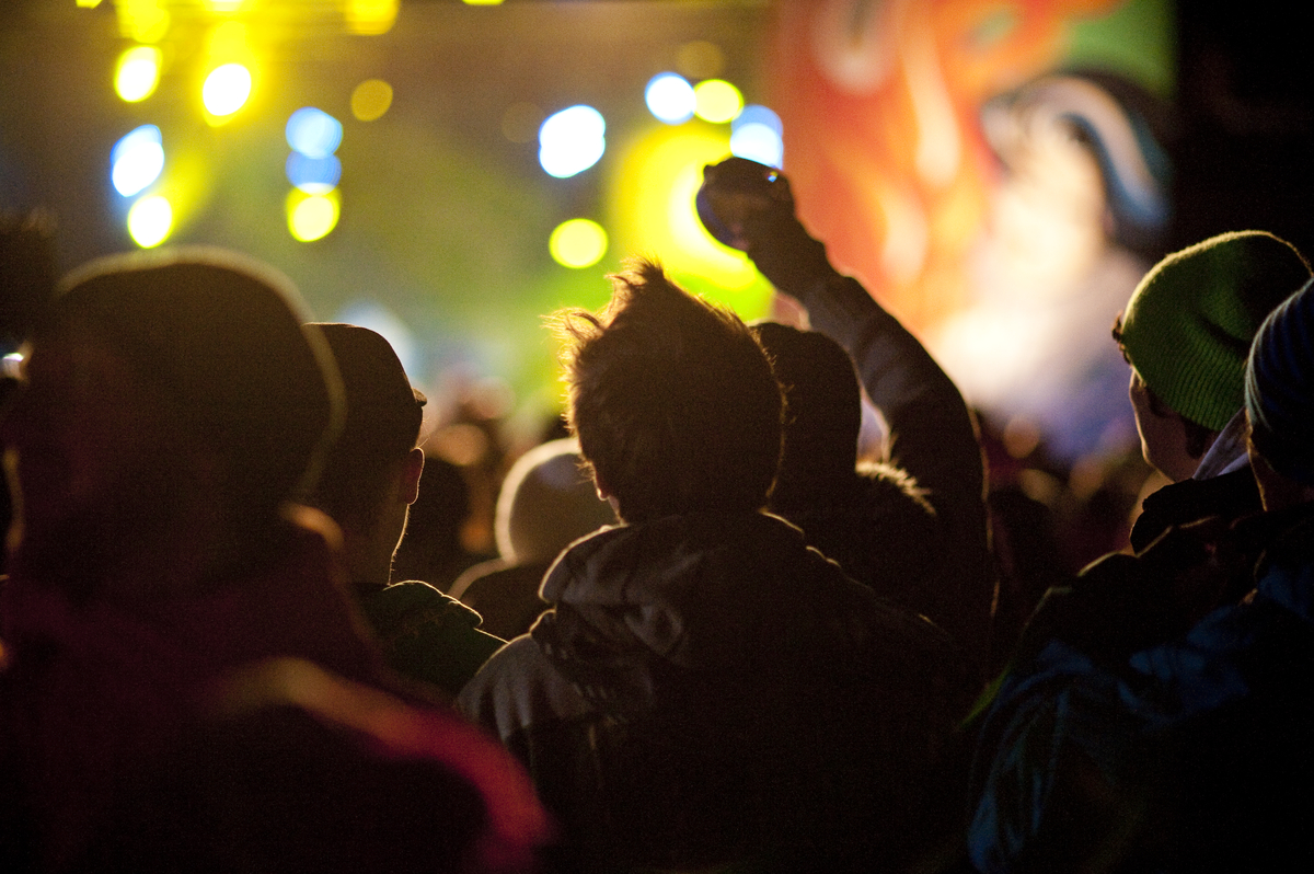 A crowd of people watches a live performance with lights and projections.